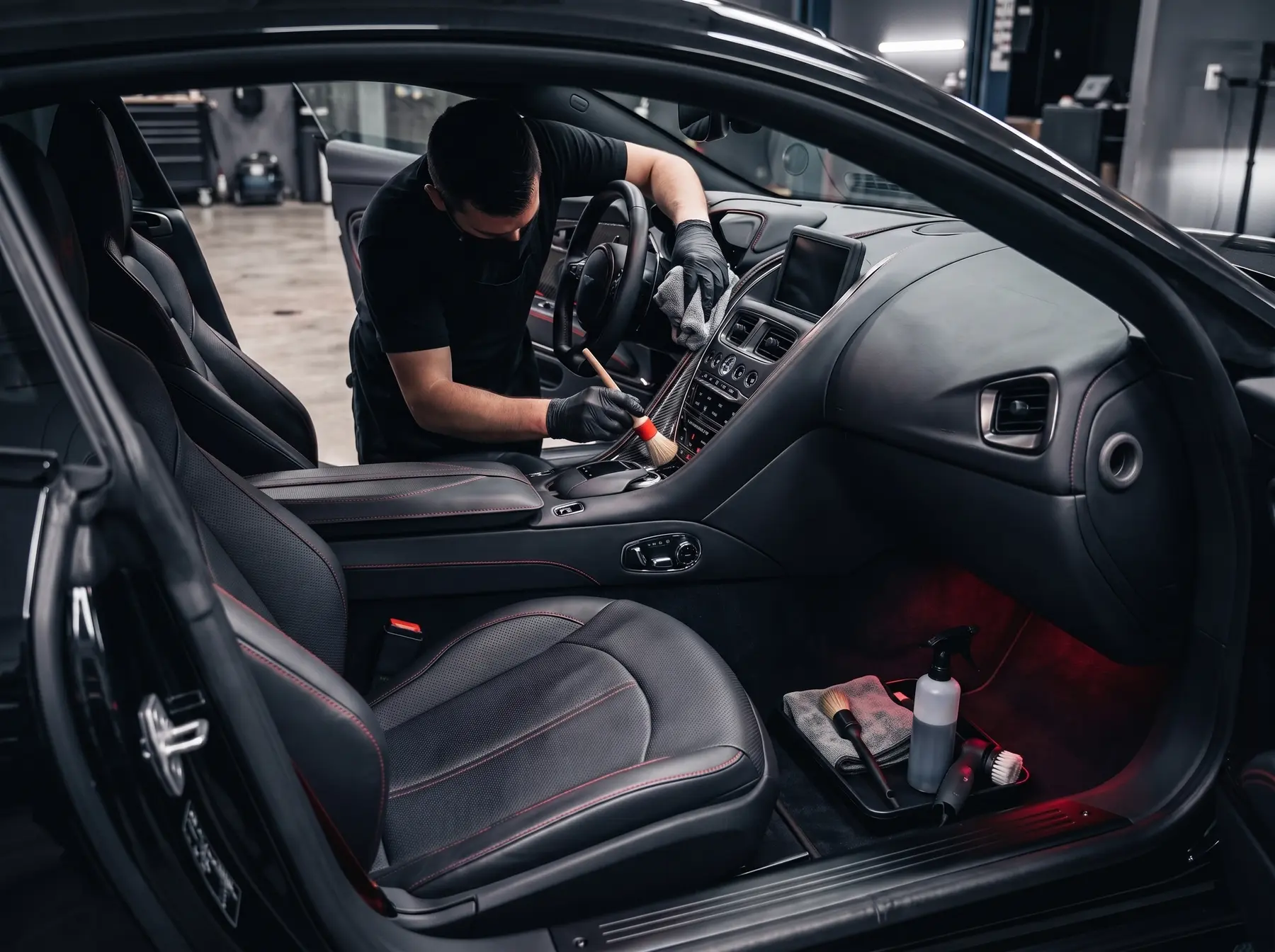 Detailer cleaning a black vehicle interior with a soft brush and microfiber cloth